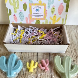 Pu&ograve; includere: Una scatola piena di carta triturata e tre saponi a forma di cactus. I saponi sono blu, verdi e gialli. La scatola &egrave; decorata con un motivo di cactus e un'etichetta che recita "Cactus Color Handmade Soaps MountainhouseSoaps Net Wt. 3.4 oz."