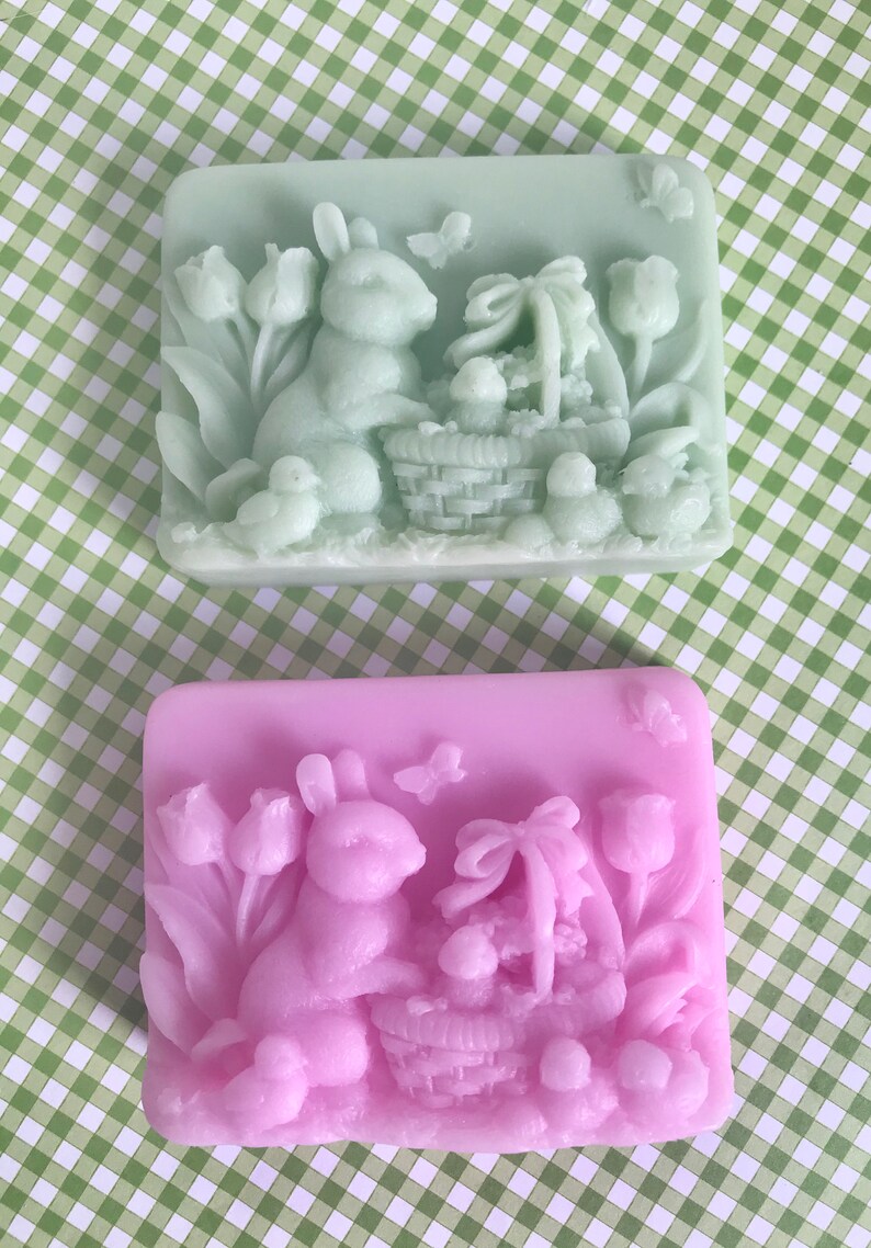 May include: Two rectangular soaps with an Easter theme. One soap is light green and the other is light purple. Both soaps feature a rabbit holding a basket of eggs and tulips.