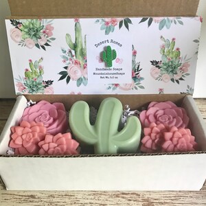 May include: A gift box filled with handmade soaps featuring a cactus and rose design. The box is decorated with a cactus and rose pattern and includes a label that reads "Desert Roses Handmade Soaps MountainhouseSoaps Net Wt. 5.0 oz".