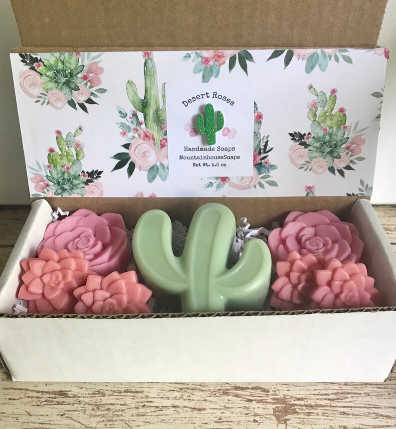 May include: A gift box filled with handmade soaps featuring a cactus and rose design. The box is decorated with a cactus and rose pattern and includes a label that reads "Desert Roses Handmade Soaps MountainhouseSoaps Net Wt. 5.0 oz".