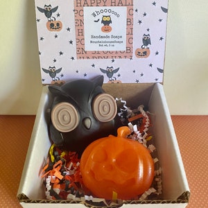 May include: A white box with a black and brown owl and an orange pumpkin soap inside. The box is decorated with a Halloween-themed pattern and a label that reads "Handmade Soaps MountainhouseSoaps Net wt. 5 oz".