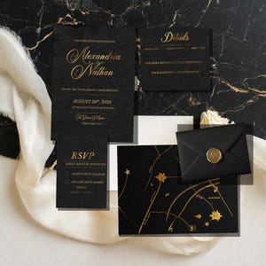 May include: A black wedding invitation suite featuring gold foil lettering and celestial map graphics. The set includes a main invitation, an RSVP card, a details card, and a black envelope sealed with a gold wax seal embossed with the letters AN.
