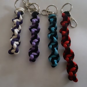 Puede incluir: Cuatro llaveros trenzados con diferentes combinaciones de colores. Los llaveros son negro y blanco, negro y morado, negro y azul, y negro y rojo.