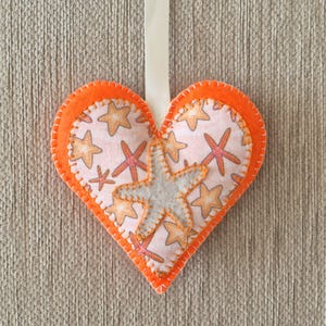 May include: Orange felt heart-shaped ornament with a white felt starfish and a white background with orange starfish print.