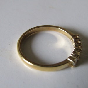 May include: A gold band ring with a row of small clear stones set into the band.