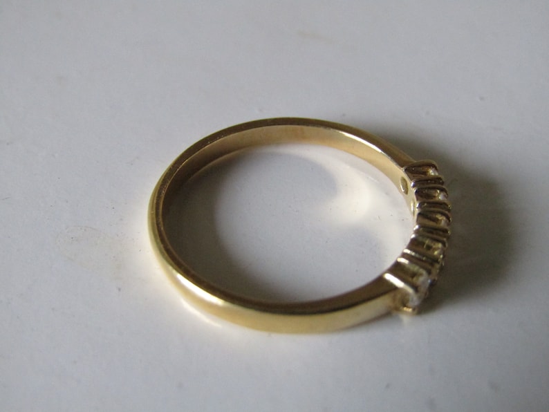 May include: A gold band ring with a row of small clear stones set into the band.