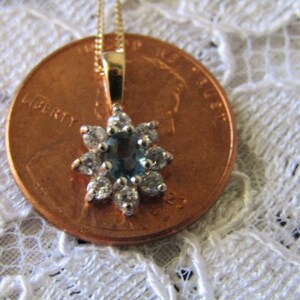 May include: A gold pendant necklace with a blue gemstone surrounded by small clear gemstones in a flower shape.