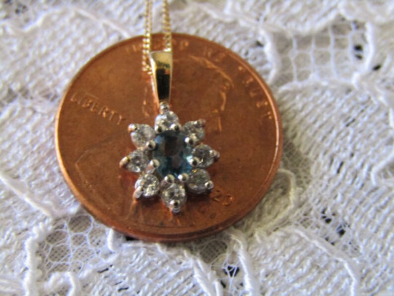 May include: A gold pendant necklace with a blue gemstone surrounded by small clear gemstones in a flower shape.