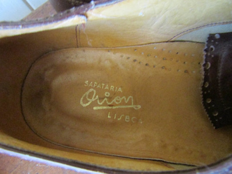 Puede incluir: Primer plano del interior de un zapato de cuero marr&oacute;n con una inscripci&oacute;n dorada que dice "SAPATARIA Orion LISBOA".
