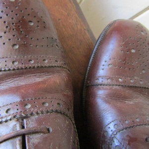 Puede incluir: Un par de zapatos de cuero marr&oacute;n con dise&ntilde;o de brogue. Los zapatos tienen cierre de cordones y punta redonda.