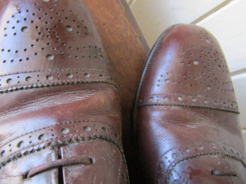 Puede incluir: Un par de zapatos de cuero marr&oacute;n con dise&ntilde;o de brogue. Los zapatos tienen cierre de cordones y punta redonda.