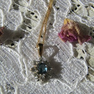 May include: A gold chain necklace with a blue gemstone pendant surrounded by smaller clear gemstones. The pendant is shaped like a star.