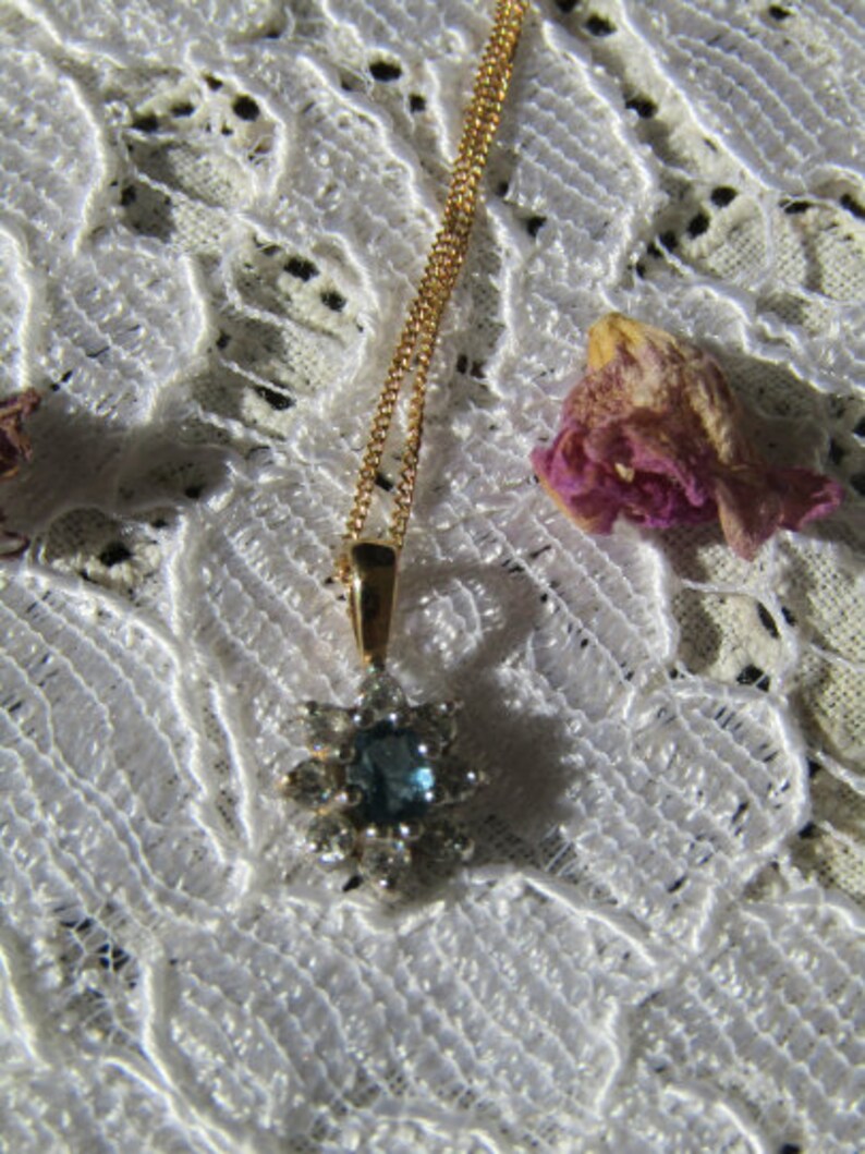 May include: A gold chain necklace with a blue gemstone pendant surrounded by smaller clear gemstones. The pendant is shaped like a star.