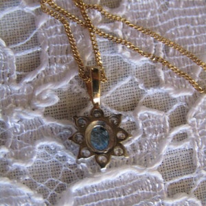 May include: A gold chain necklace with a pendant featuring a blue gemstone surrounded by smaller clear gemstones.