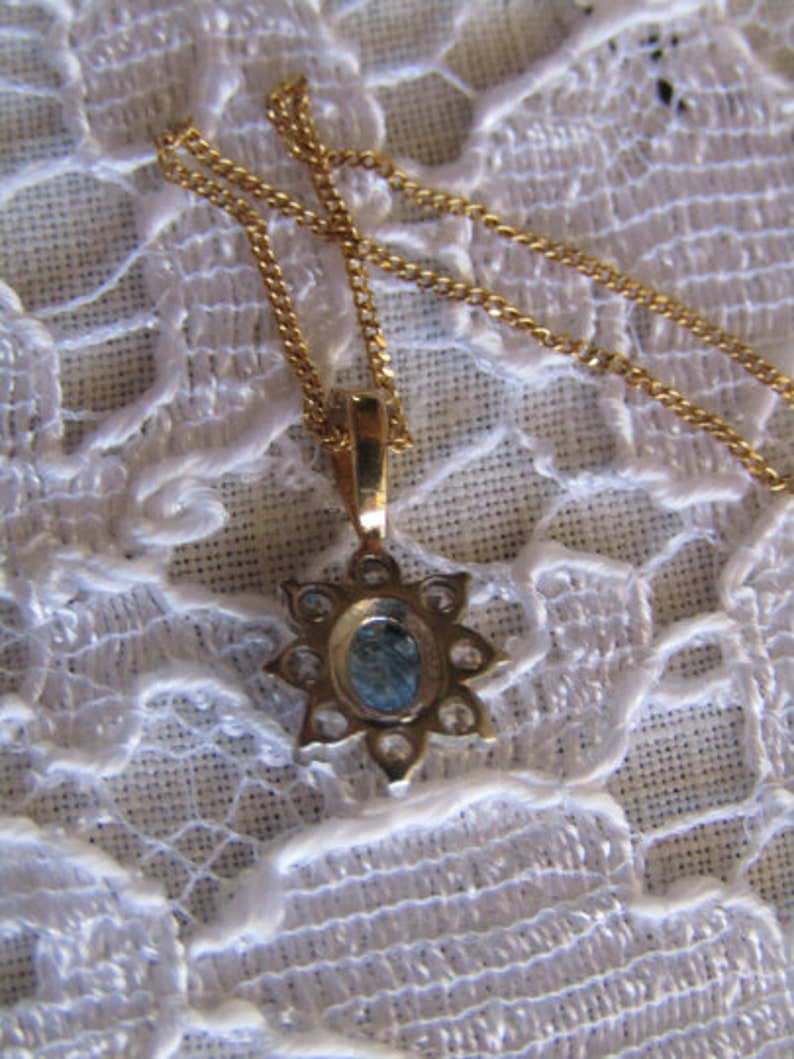 May include: A gold chain necklace with a pendant featuring a blue gemstone surrounded by smaller clear gemstones.