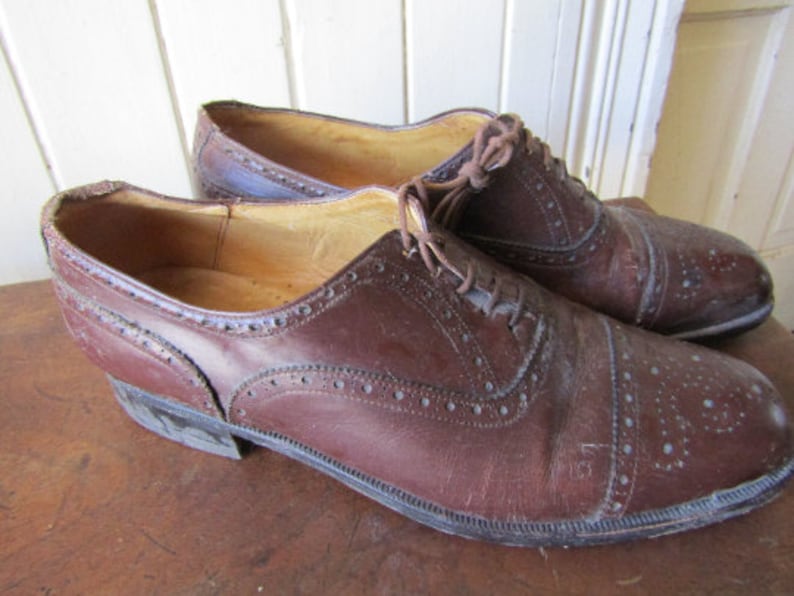 Puede incluir: Un par de zapatos de cuero marr&oacute;n con dise&ntilde;o de punta de ala. Los zapatos tienen cierre de cordones y punta redonda.