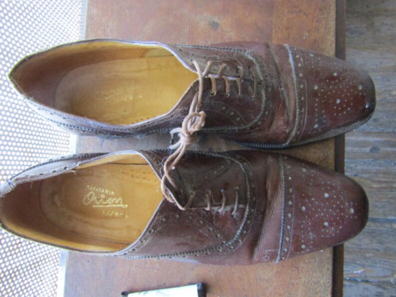 Puede incluir: Un par de zapatos de cuero marr&oacute;n con un dise&ntilde;o de cordones y un patr&oacute;n perforado. Los zapatos tienen una etiqueta que dice "Sapataria Orion".