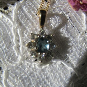 May include: A gold chain necklace with a pendant featuring a blue gemstone surrounded by smaller clear gemstones.