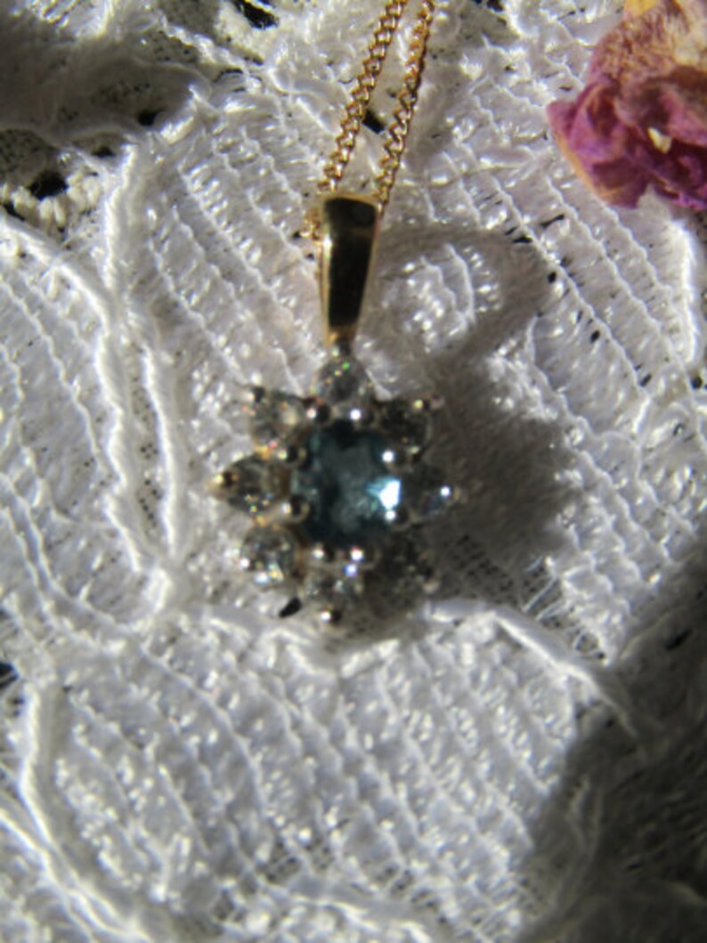 May include: A gold chain necklace with a pendant featuring a blue gemstone surrounded by smaller clear gemstones.