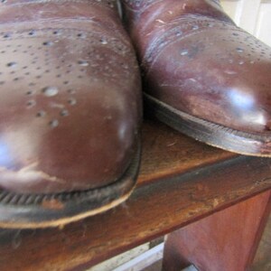 Puede incluir: Un par de zapatos de cuero marr&oacute;n con detalles de brogue. Los zapatos tienen un aspecto desgastado y est&aacute;n hechos de cuero liso.
