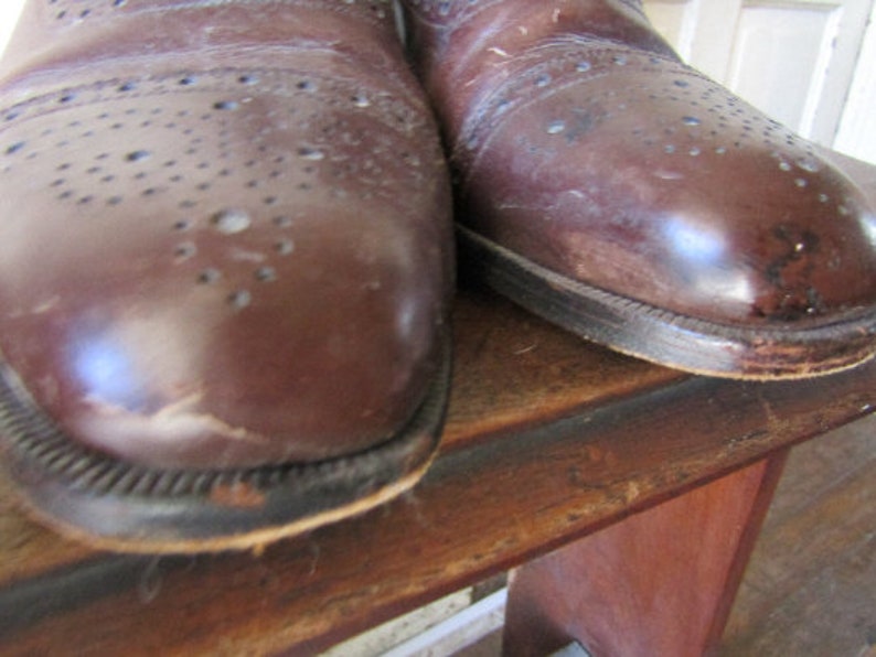 Puede incluir: Un par de zapatos de cuero marr&oacute;n con detalles de brogue. Los zapatos tienen un aspecto desgastado y est&aacute;n hechos de cuero liso.