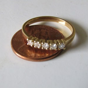 May include: A gold band ring with five small diamonds set in a row. The ring is placed on top of a US penny.