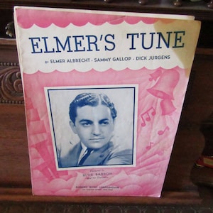 May include: A vintage sheet music cover for the song "Elmer's Tune" featuring a photo of Blue Barron and his orchestra. The cover is pink with white scalloped edges and features musical notes and bells.