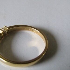 May include: A gold band ring with a row of small clear stones set in the band. The inside of the band is marked "14K" and "G74".
