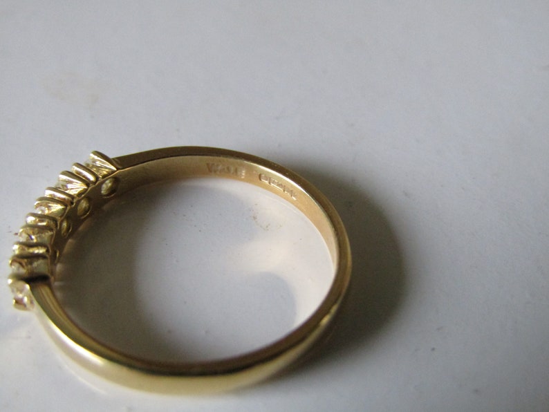 May include: A gold band ring with a row of small clear stones set in the band. The inside of the band is marked "14K" and "G74".