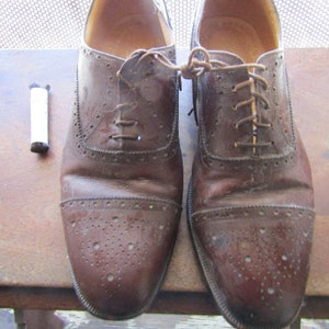 Puede incluir: Un par de zapatos Oxford de cuero marr&oacute;n con cordones. Los zapatos tienen un dise&ntilde;o de brogue y est&aacute;n usados.