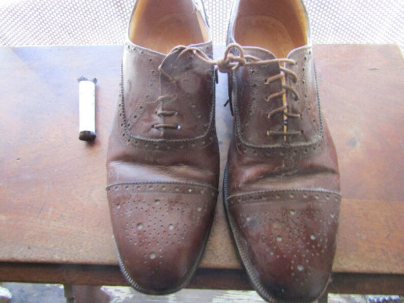 Puede incluir: Un par de zapatos Oxford de cuero marr&oacute;n con cordones. Los zapatos tienen un dise&ntilde;o de brogue y est&aacute;n usados.