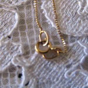 May include: A gold chain necklace with a delicate, interlocking circle pendant. The chain is visible against a white lace background.