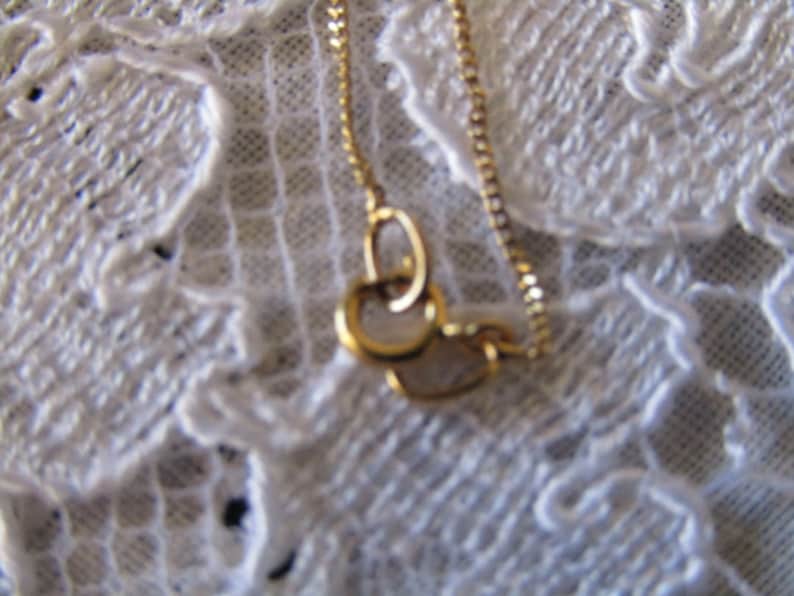 May include: A gold chain necklace with a delicate, interlocking circle pendant. The chain is visible against a white lace background.