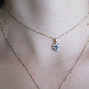 May include: A gold chain necklace with a delicate pendant featuring a blue gemstone surrounded by smaller clear gemstones.