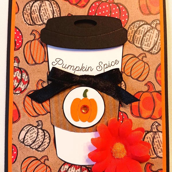 Puede incluir: Tarjeta de felicitación hecha a mano con temática otoñal. La tarjeta presenta un diseño de taza de café con las palabras "Pumpkin Spice" y un gráfico de calabaza. Una cinta negra y una flor naranja añaden detalles. El fondo está estampado con calabazas.