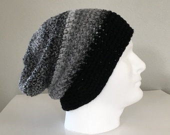May include: A slouchy crochet beanie hat featuring a gradient color pattern that transitions from a solid black brim to shades of dark gray, medium gray, and light gray at the crown. The textured knit construction displays a consistent stitch pattern.