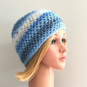 May include: A blue and white crocheted beanie hat with a loose, open weave. The hat is worn by a person with blonde hair.