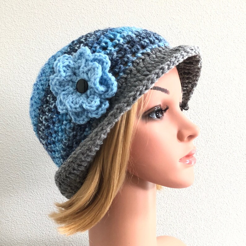 Puede incluir: Un gorro de punto azul y gris con una flor de punto azul en el lateral.
