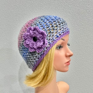 May include: A purple and blue crocheted beanie with a purple crocheted flower on the side.