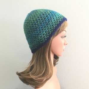 May include: A green and blue crocheted beanie with a navy blue brim. The beanie is on a mannequin head with long brown hair.