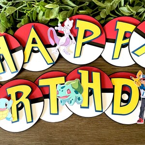 K&ouml;nnte beinhalten: Ein Happy Birthday Banner mit kreisf&ouml;rmigen rot-wei&szlig;en Pok&eacute;ball-Ausschnitten als Hintergrund f&uuml;r gro&szlig;e gelbe Buchstaben. Das Design enth&auml;lt verschiedene Zeichentrickfiguren, darunter Mewtu, Schiggy, Bisasam sowie Ash mit Pikachu.