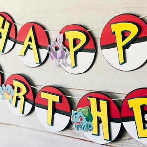 K&ouml;nnte beinhalten: Ein dekoratives Banner mit der Aufschrift HAPPY BIRTHDAY, bestehend aus gelben Buchstaben auf runden, rot-wei&szlig;-schwarzen Pok&eacute;ball-Designs. Das Banner enth&auml;lt Ausschnitte verschiedener animierter Charaktere wie Ash Ketchum, Mewtwo, Squirtle, Bulbasaur und Pikachu.