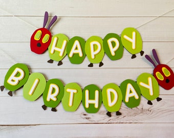 May include: A two-row paper banner spelling HAPPY BIRTHDAY. Each letter is on a green caterpillar body segment. The banner features red caterpillar heads with purple antennae and yellow eyes at the start and end, with small brown feet attached.