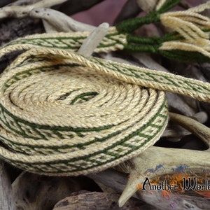 May include: A close-up of a coiled, woven, green and cream-colored strap. The strap is made of a natural fiber and has a decorative pattern. The strap is lying on a piece of wood.
