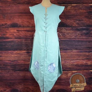 May include: A light blue tunic with a lace-up front and two embroidered designs on the bottom. The tunic has short, capped sleeves and a V-neck.