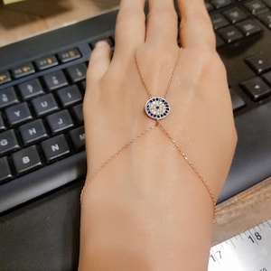 May include: A rose gold chain bracelet with an evil eye charm. The charm is round and features a blue eye with white stones surrounding it.