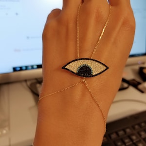 May include: A gold chain bracelet with a blue and black evil eye charm. The charm is covered in sparkling rhinestones.