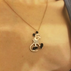 May include: A gold chain necklace with a black and white Mickey Mouse pendant. The pendant is made of metal and has a shiny finish.