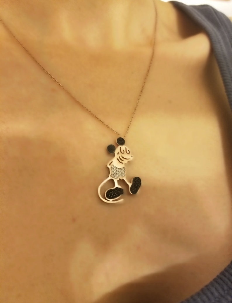 May include: A gold chain necklace with a black and white Mickey Mouse pendant. The pendant is made of metal and has a shiny finish.