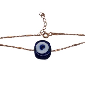 May include: A rose gold chain bracelet with a blue and white evil eye charm. The charm is round and has a white center with a blue eye in the middle.